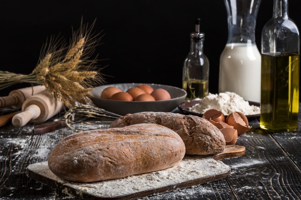 beautiful still life with different kinds bread grain flour weight ears wheat pitcher milk eggs black background